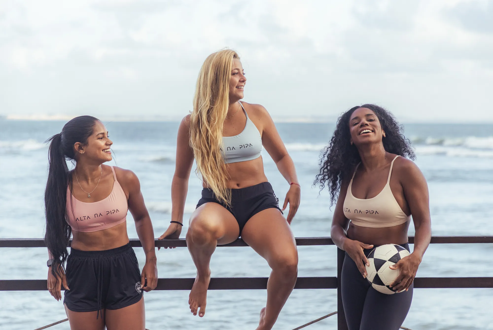 Três alunas sorrindo na beira do mar com a bola de altinha