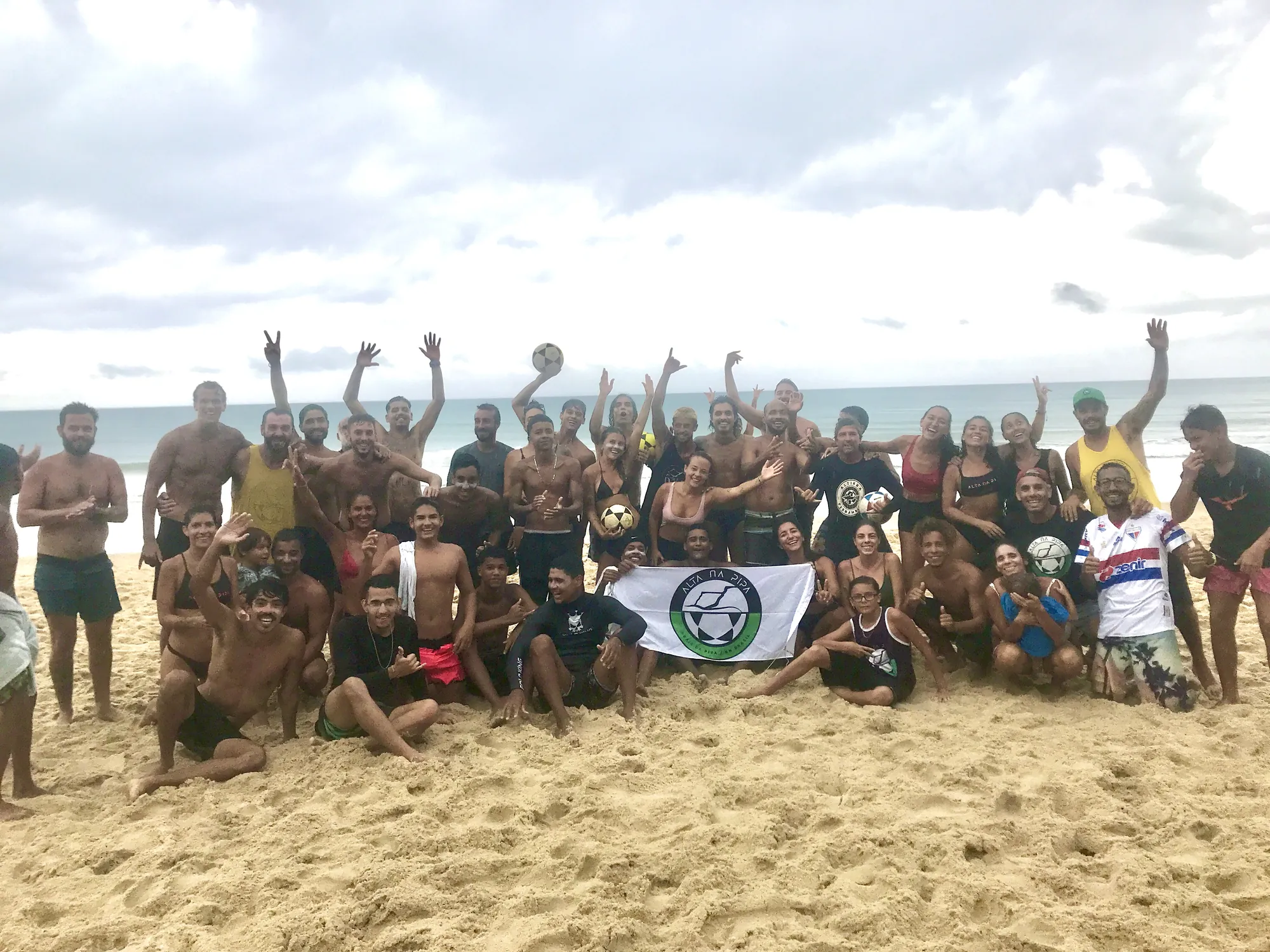 Grupo de alunos na praia com a bandeira da Alta na Pipa