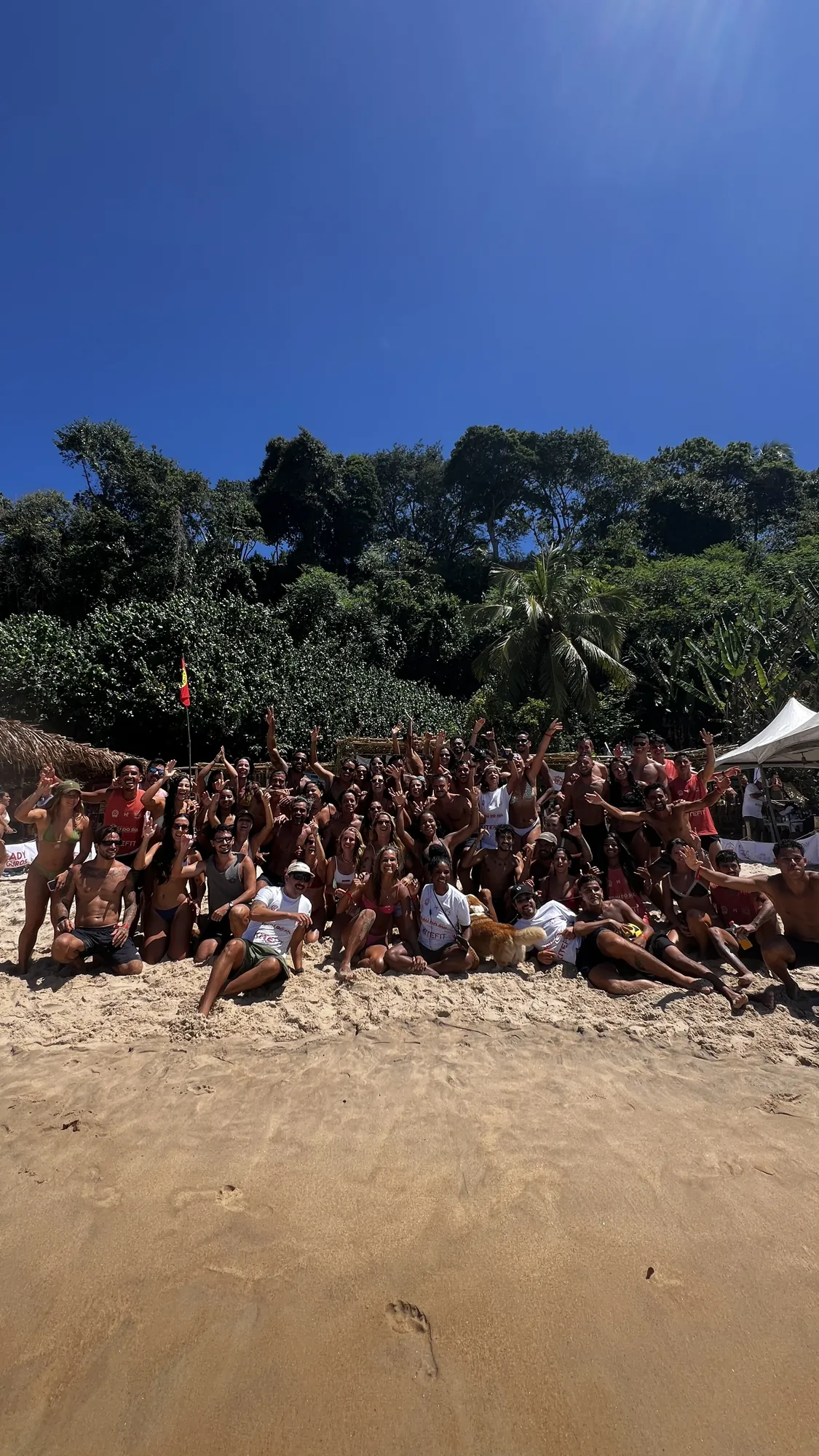 Grupo grande reunido na areia sob o céu azul